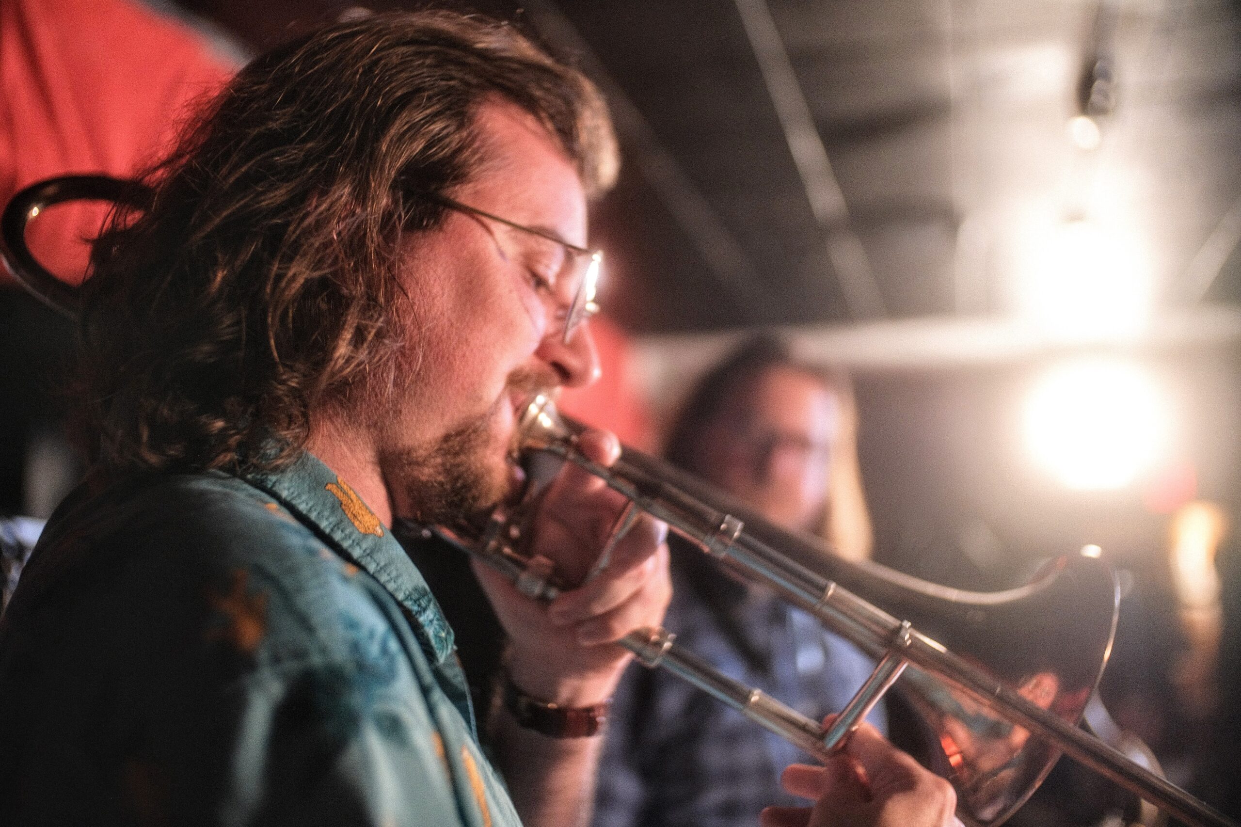 A person with light skin and long brown hair plays a trombone.