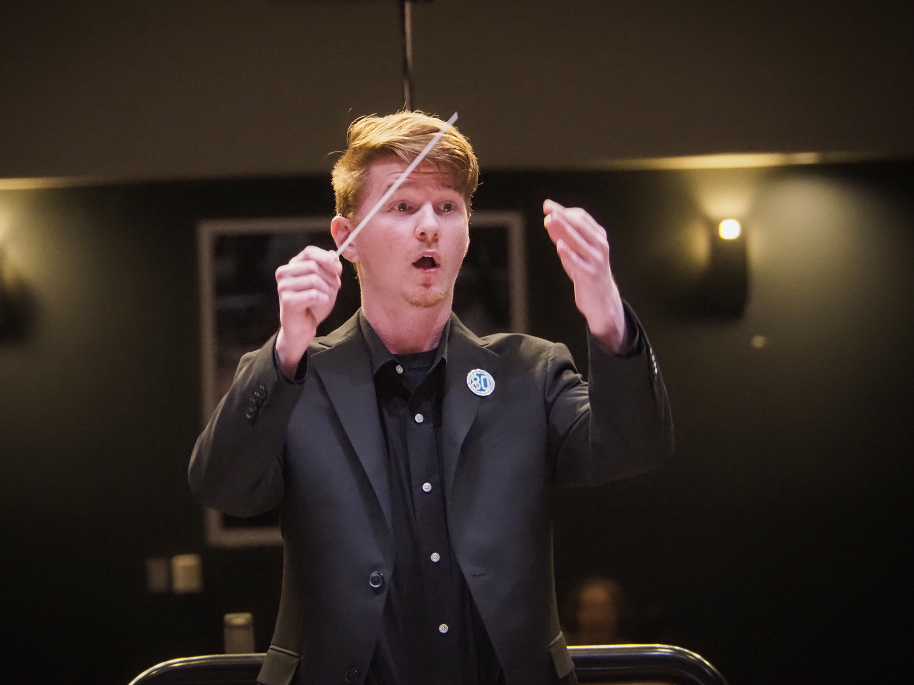 A man with light skin and blond hair conducting music.