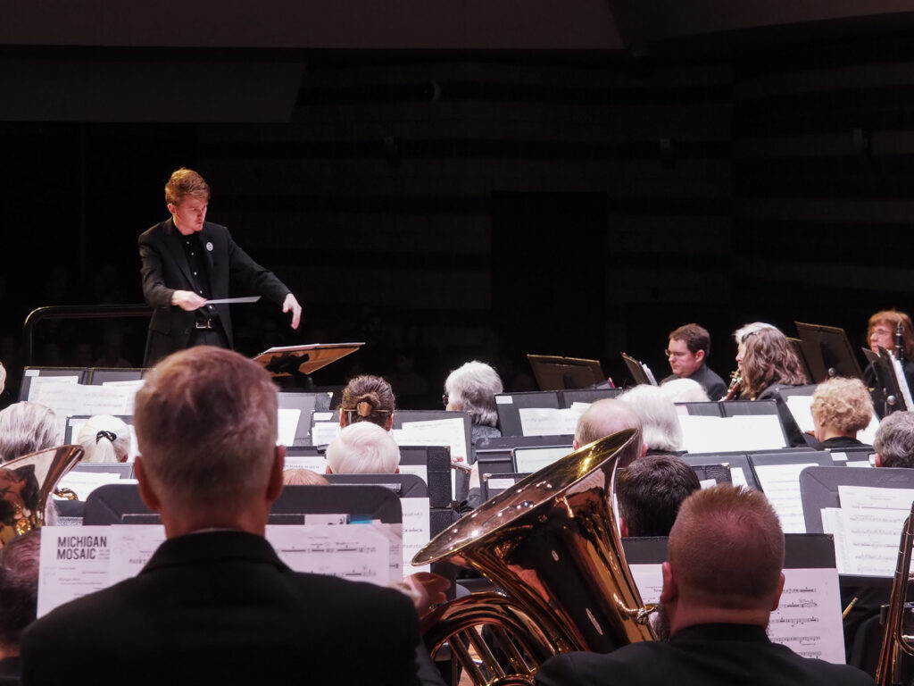 A conductor in front of many musicians with stands.