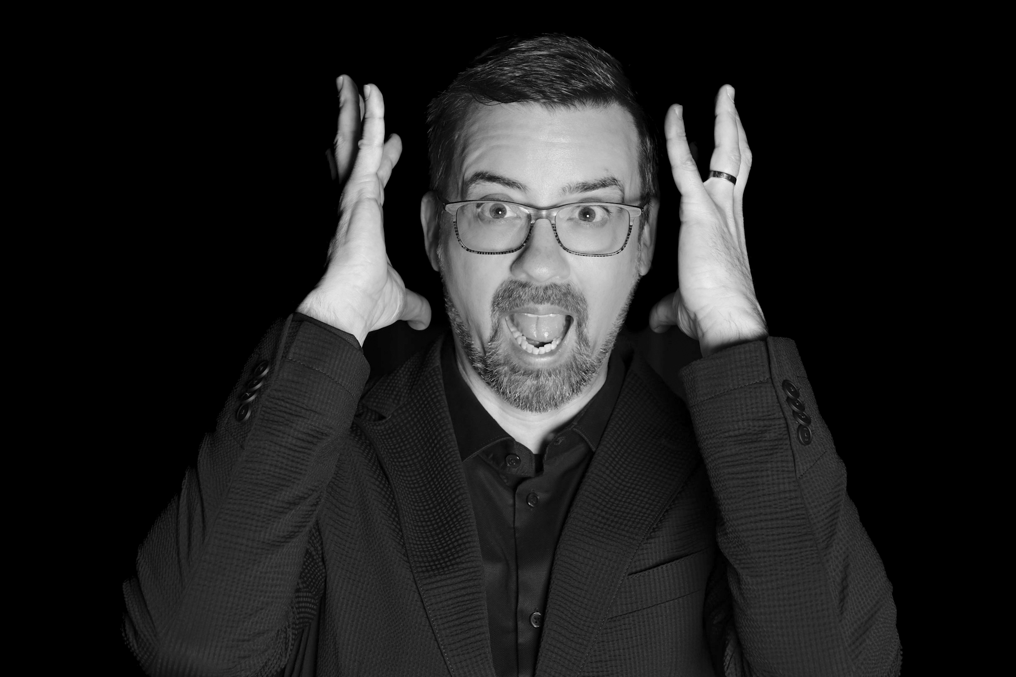 A man with an open mouth and wide eyes hovering his hands over his ears.