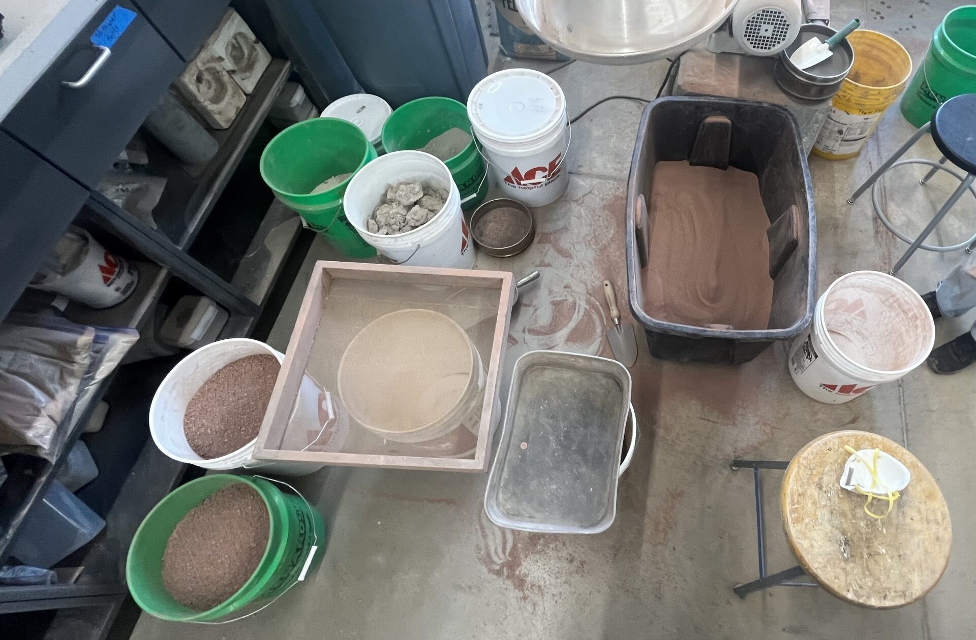 Many buckets holding clay and water sitting on a floor.