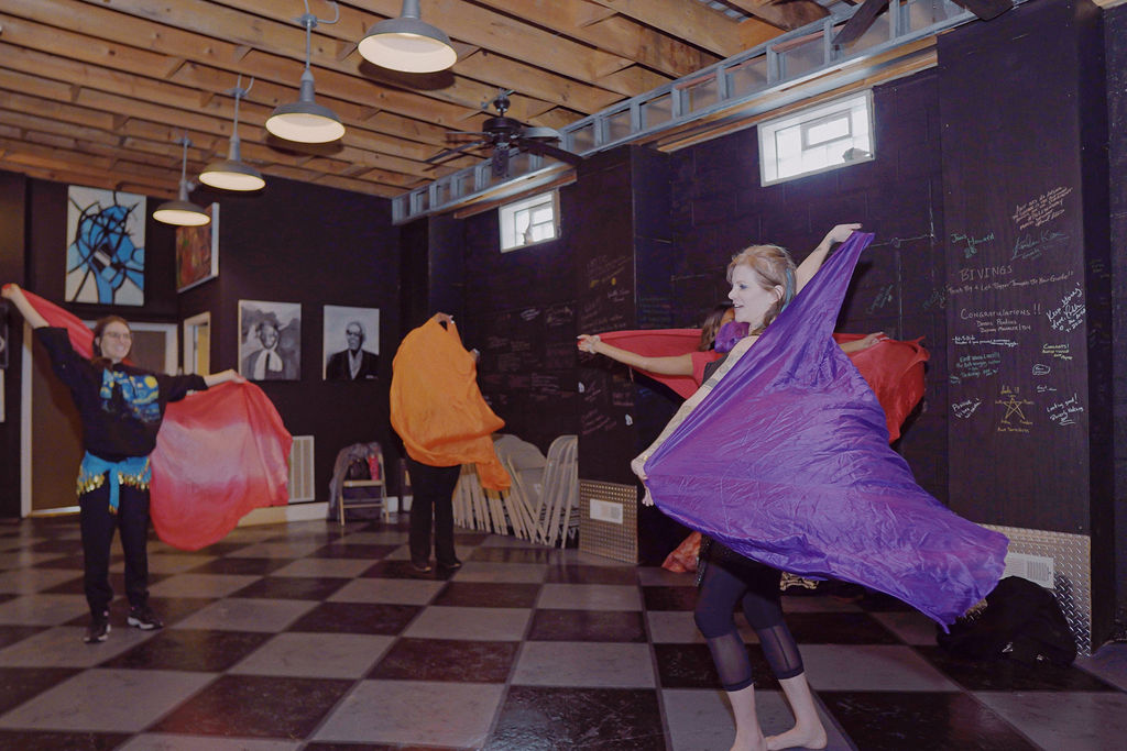 Four people moving their bodies while holding large flowly fabric