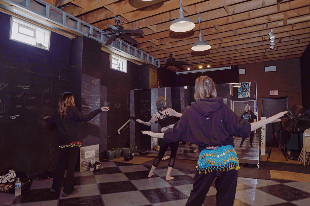 Three people facing a large mirror as they move their bodies during a bellydance workshop