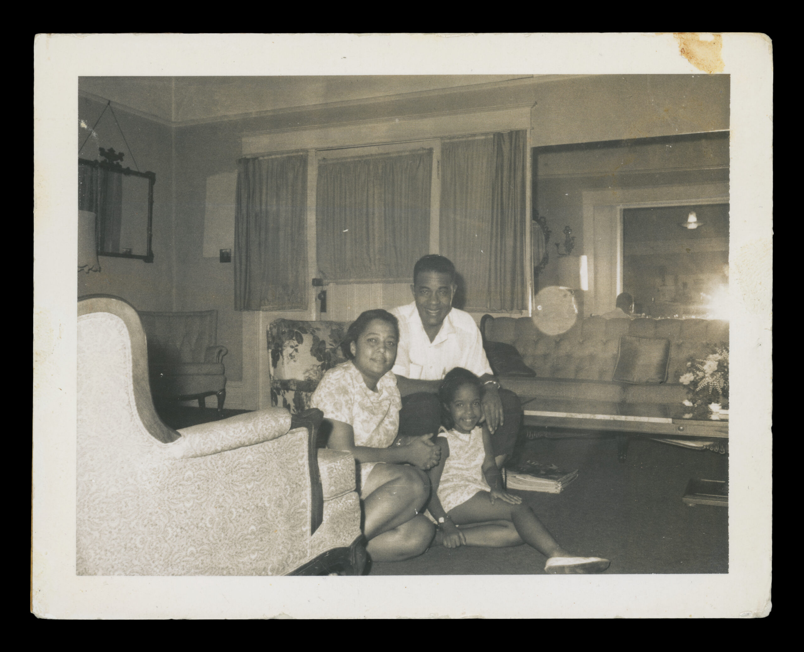 A black and white archival family photo of two adults and a young child in their living room