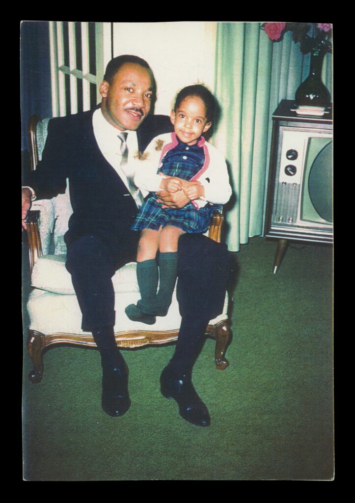 An archival photo of an adult wearing a suit holding a young child on their lap as they sit on an armchair