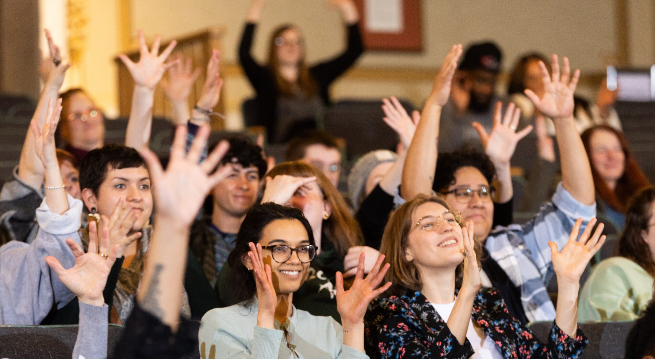 Audience members raise their hands and smile broadly during an interactive event.