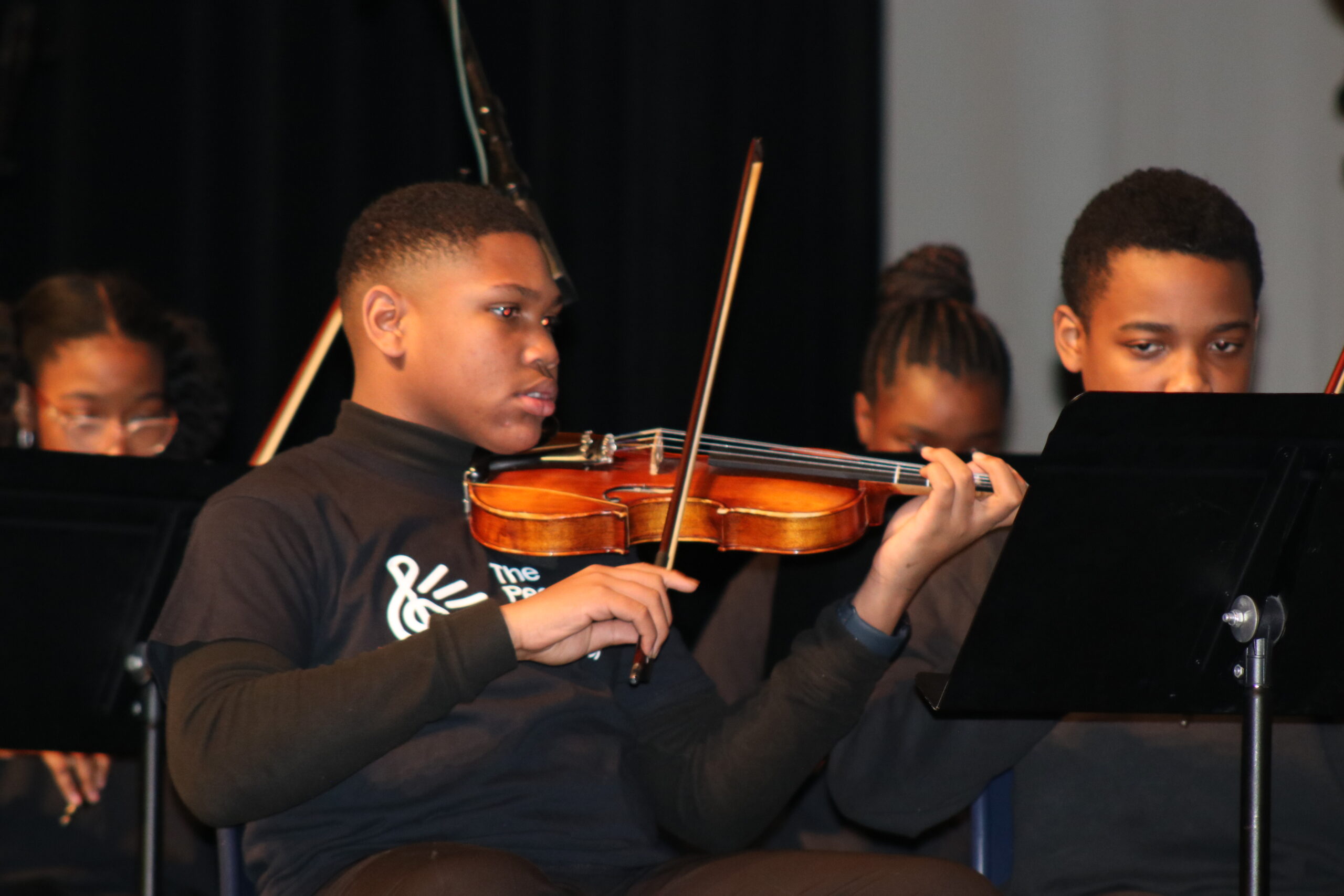 A young musician playing the violin with other performers