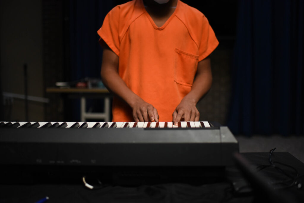 A young person playing an electric keyboard on a darkened stage.
