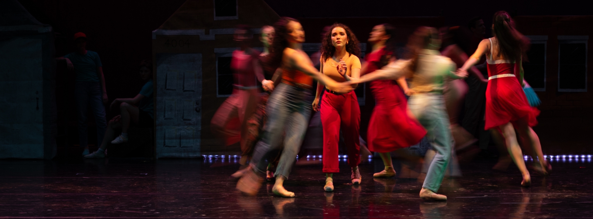 Ballet dancers on stage in contemporary clothing circling around the lead character.