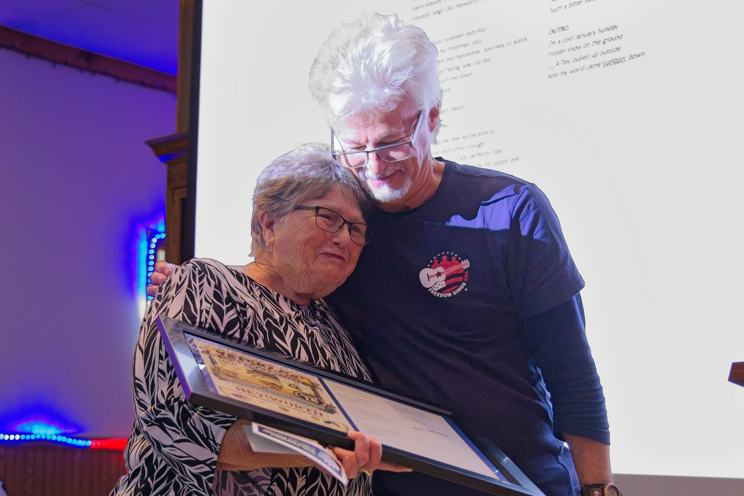 Two people embracing and holding a plaque.