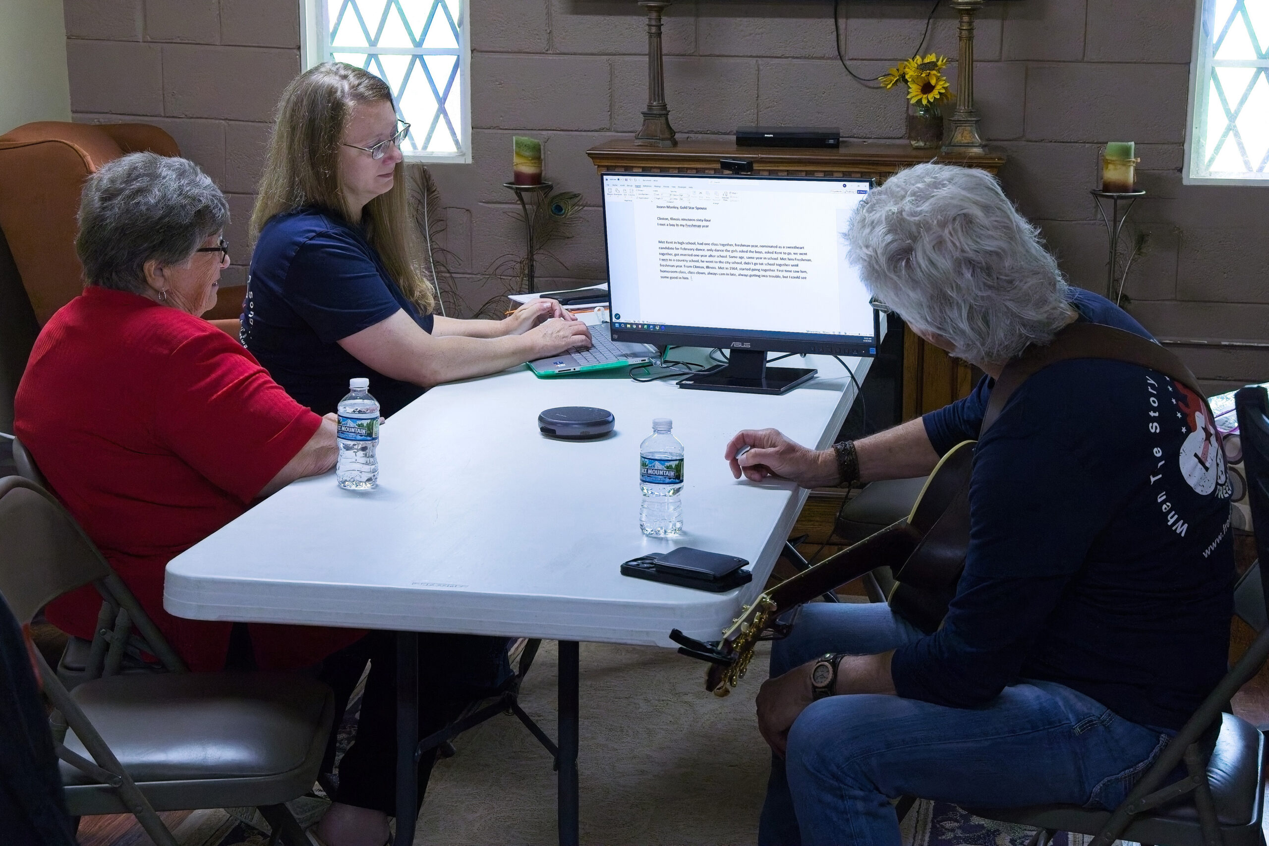 Three people sitting around a folding card table looking at a computer monitor.