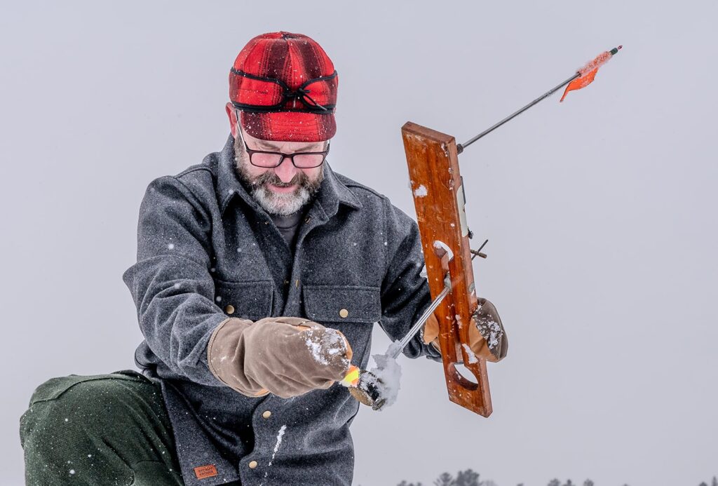 A person wearing a woolen red and black plaid brimmed cap with a band around it. They are holding an equipment for ice fishing.