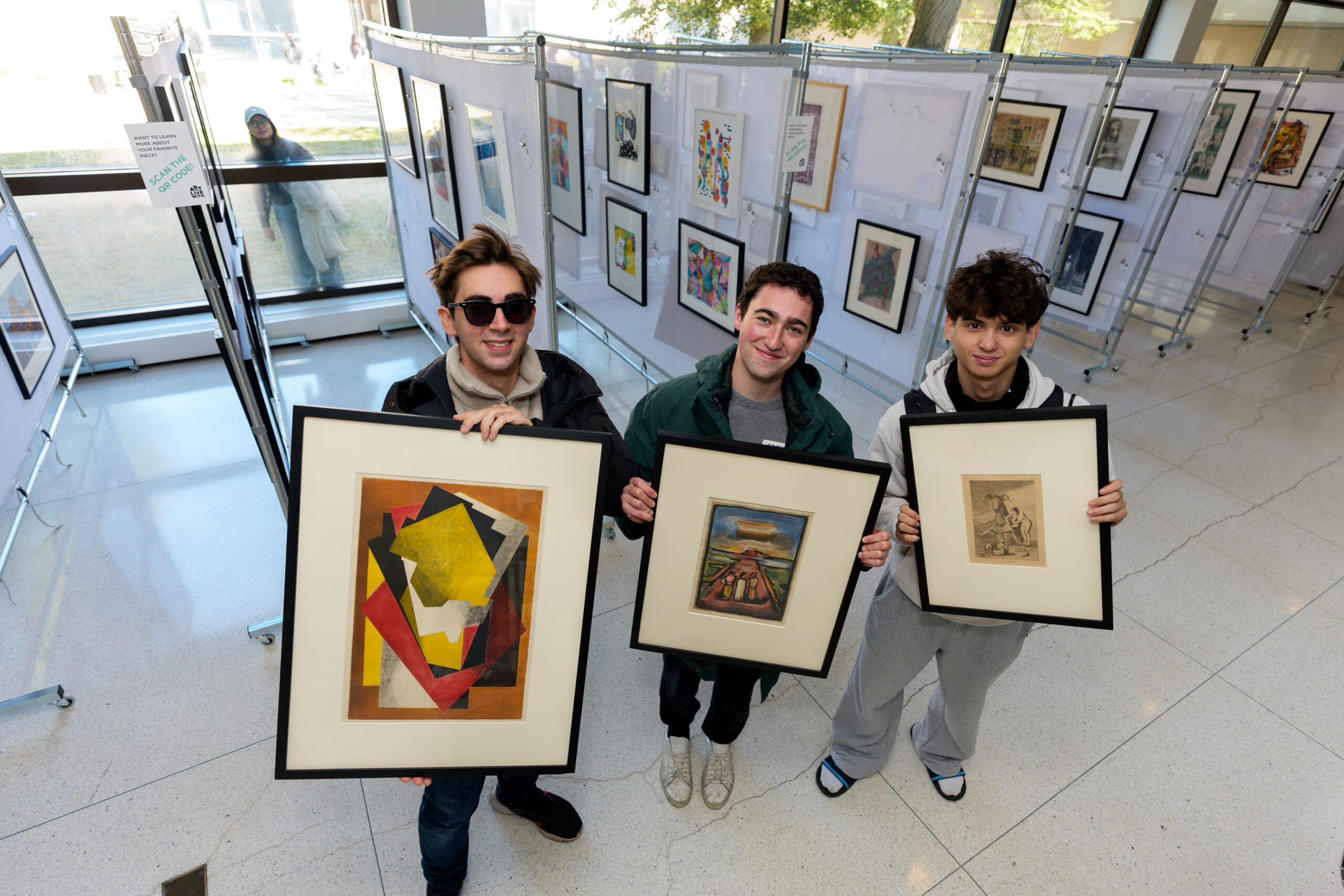 Three people holding framed artworks