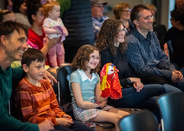 An audience smiling with a young girl holding a puppet.