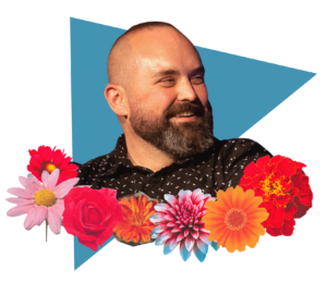 Headshot of a smiling person with light skin tone, close-cropped hair and dark beard, wearing a black shirt, set against a blue triangle and framed by colorful flowers.