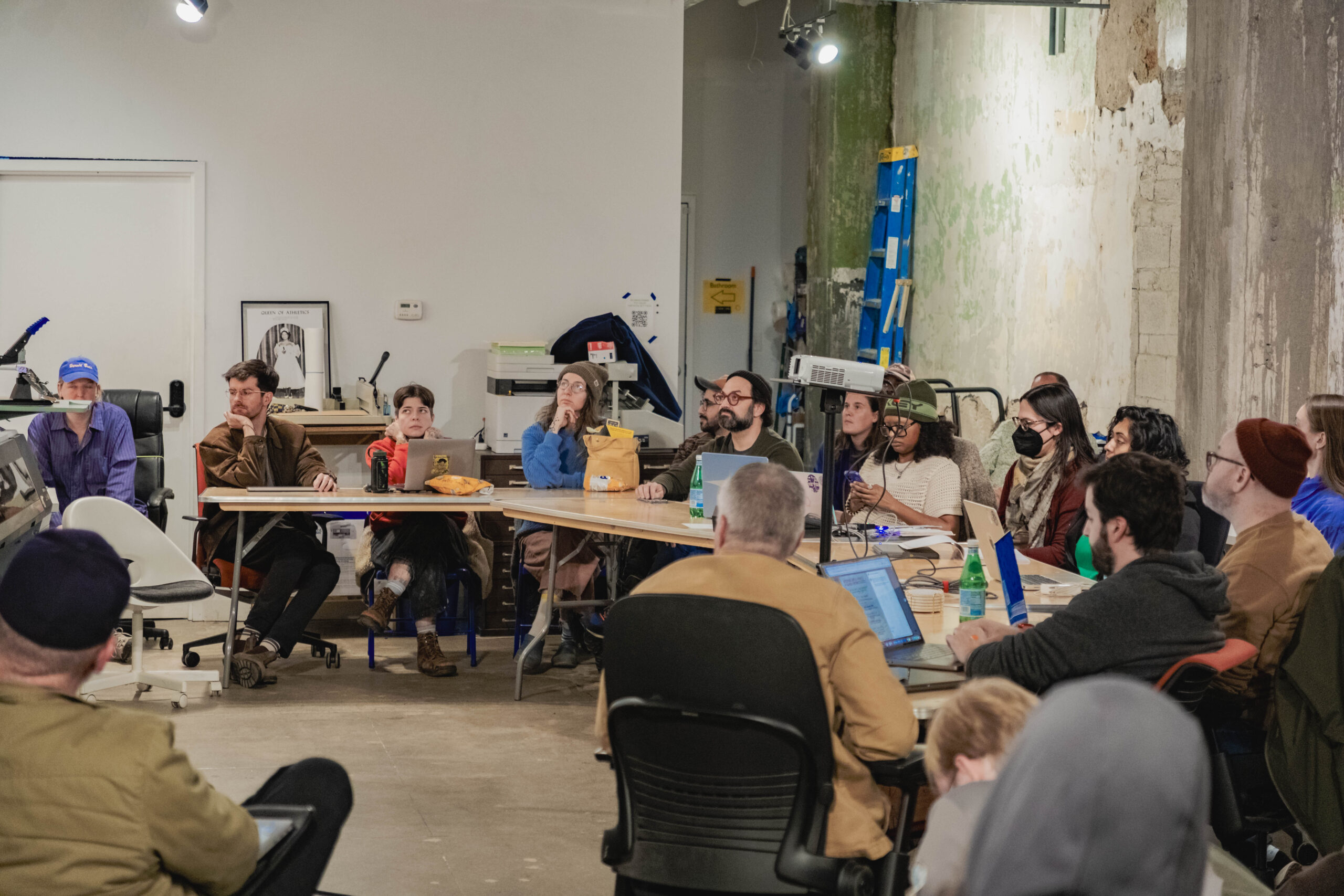 People with laptops sitting at a long table looking off to the side.