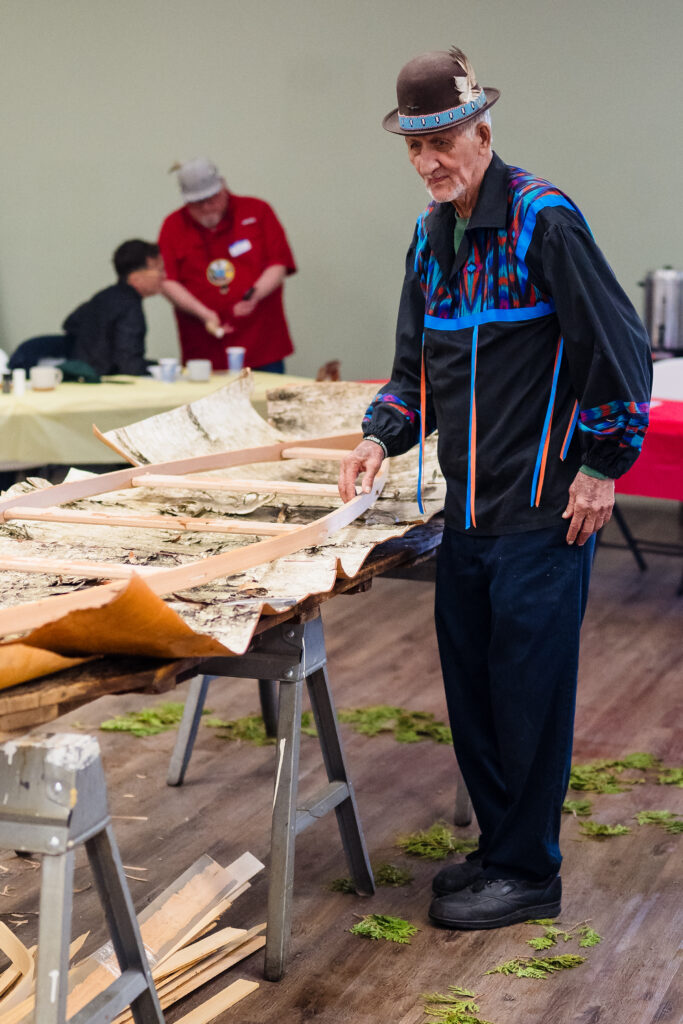 A person standing by a table with birch bark and a canoe frame
