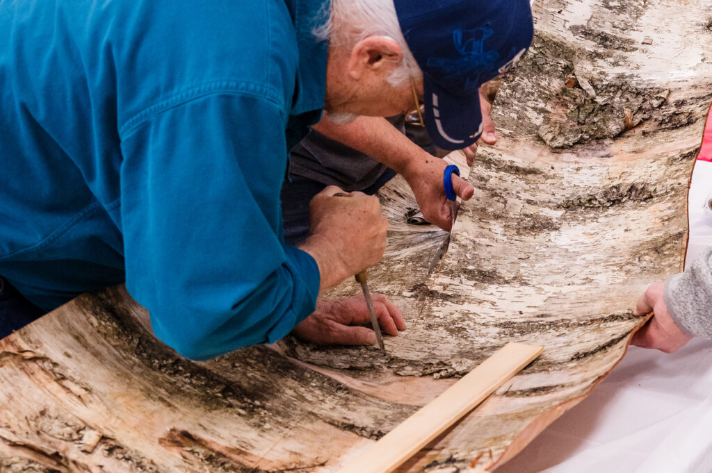 A close up of people working on scoring and cutting birch bark on a table