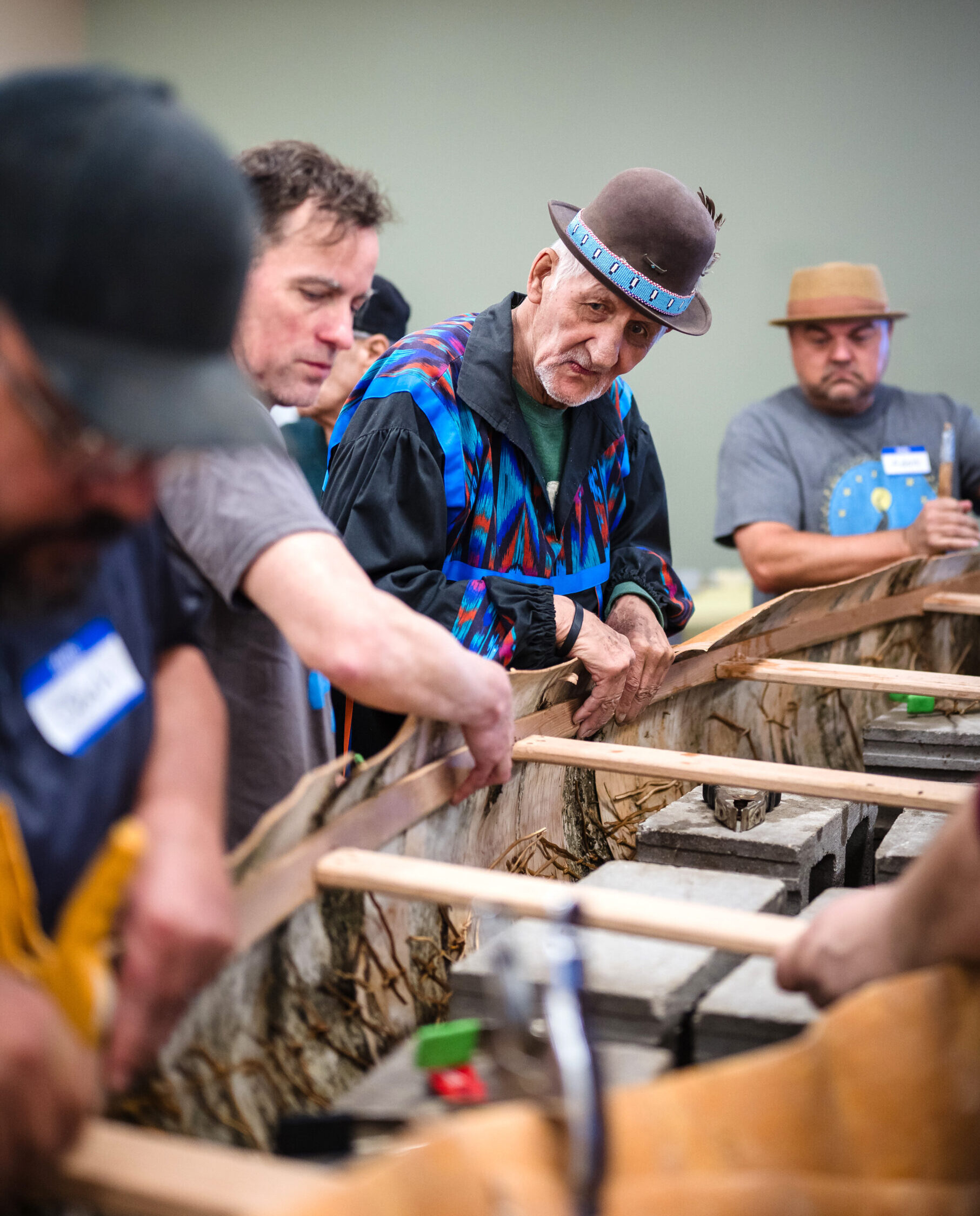 A group of people standing and holding together layers of birch bark and a canoe frame as they build the canoe together
