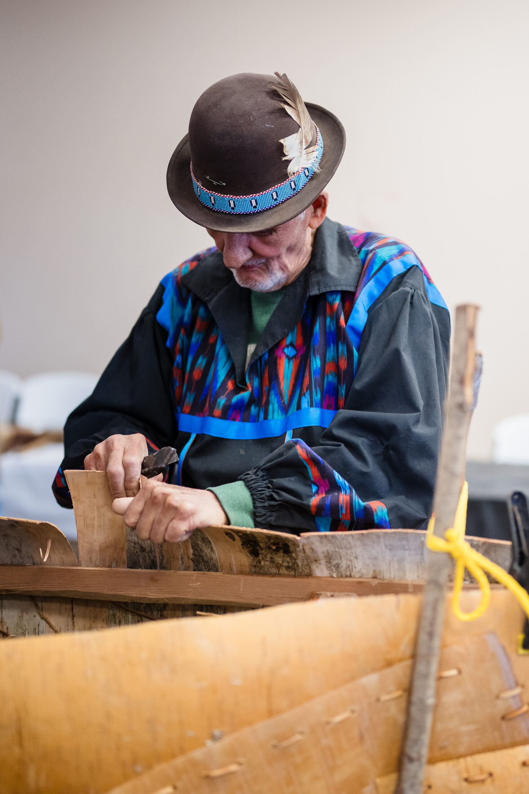 A person wearing a hat and colorful shirt working on a birch bark canoe build