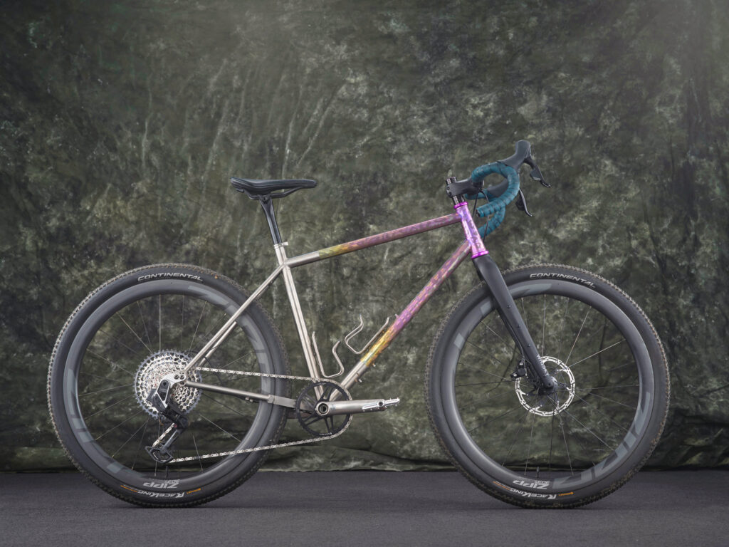 A bicycle with a silvery metal frame and other colorful embellishments on the cross bars and handles.