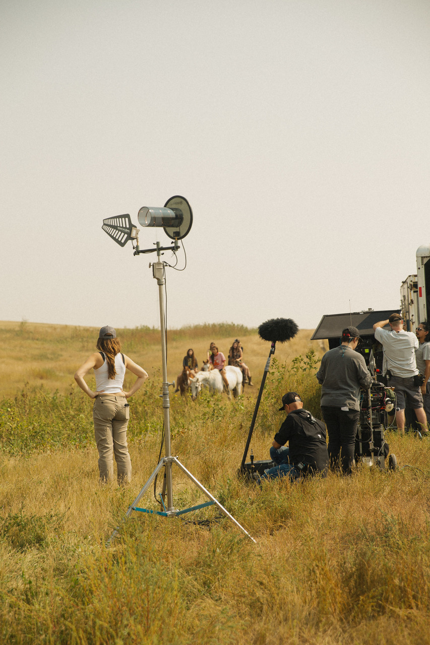 A film crew filming a group of young adults on horses in an open field