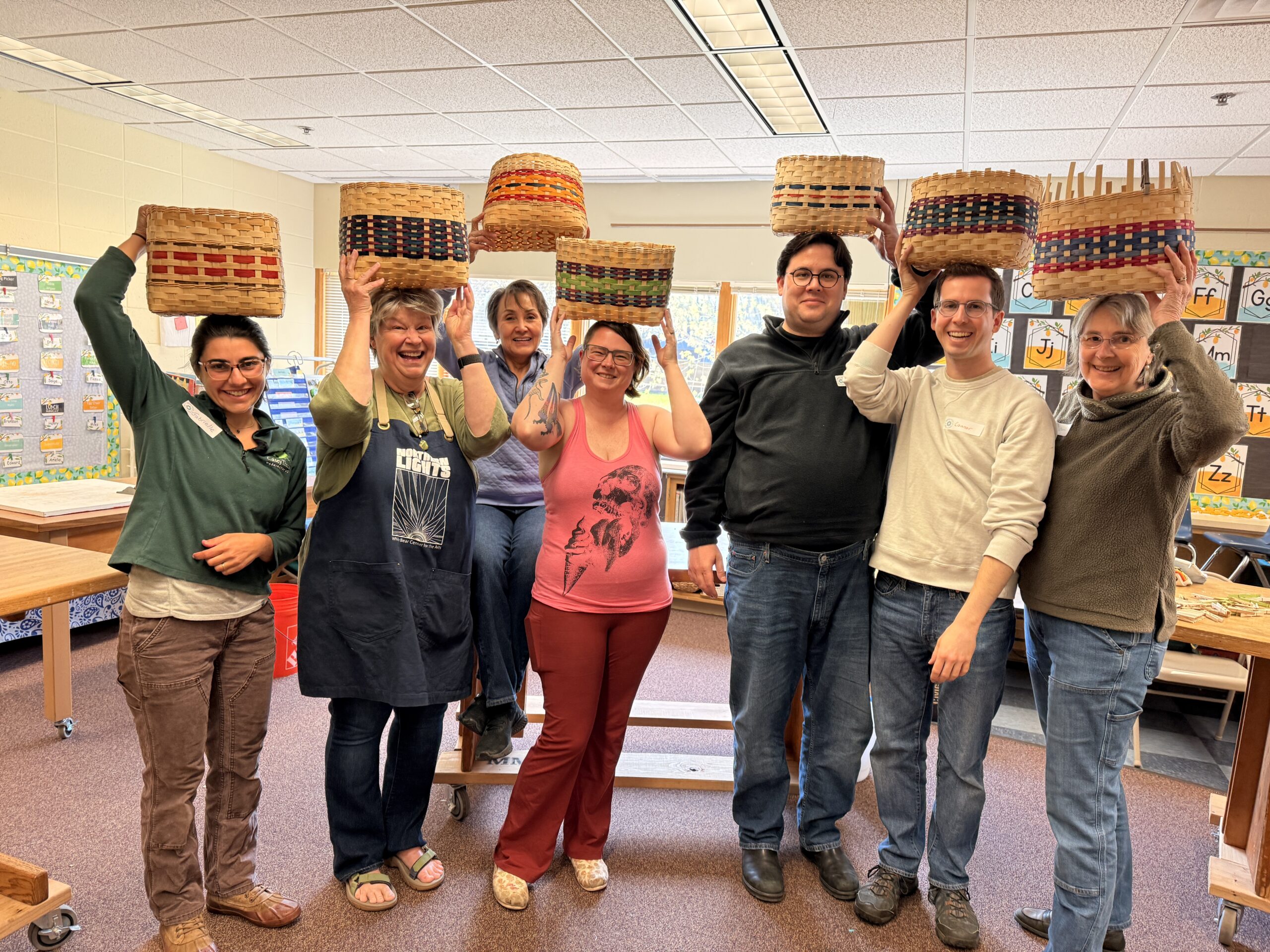 Seven people smiling and posing with handmade bike baskets on their heads.