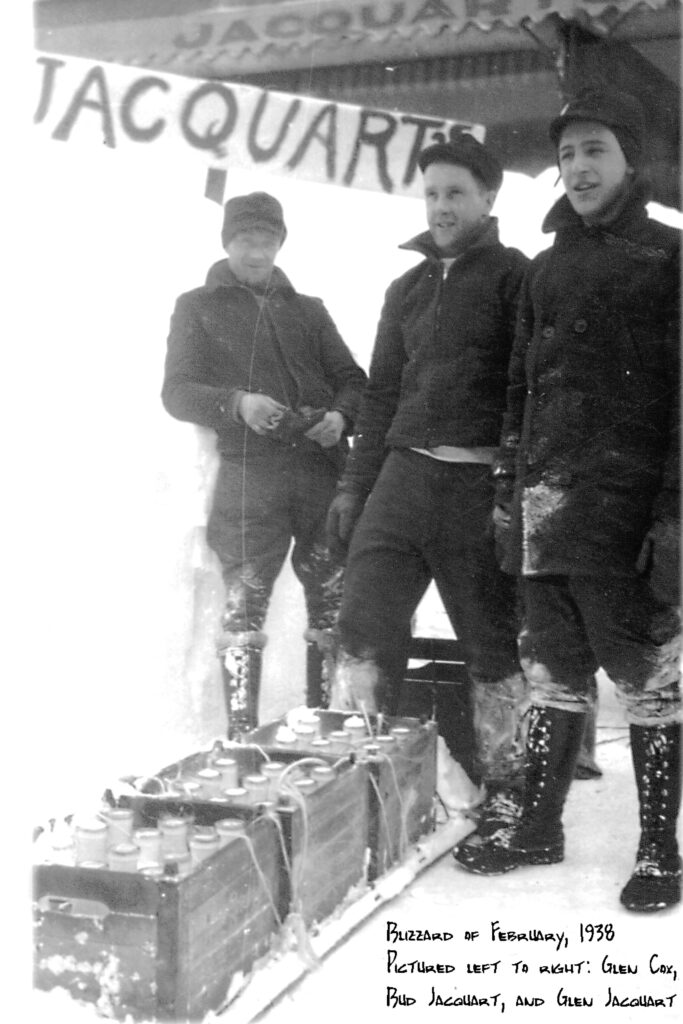 A black and white archival photo of three people wearing woolens and brimmed caps as they stand in wintery outdoors