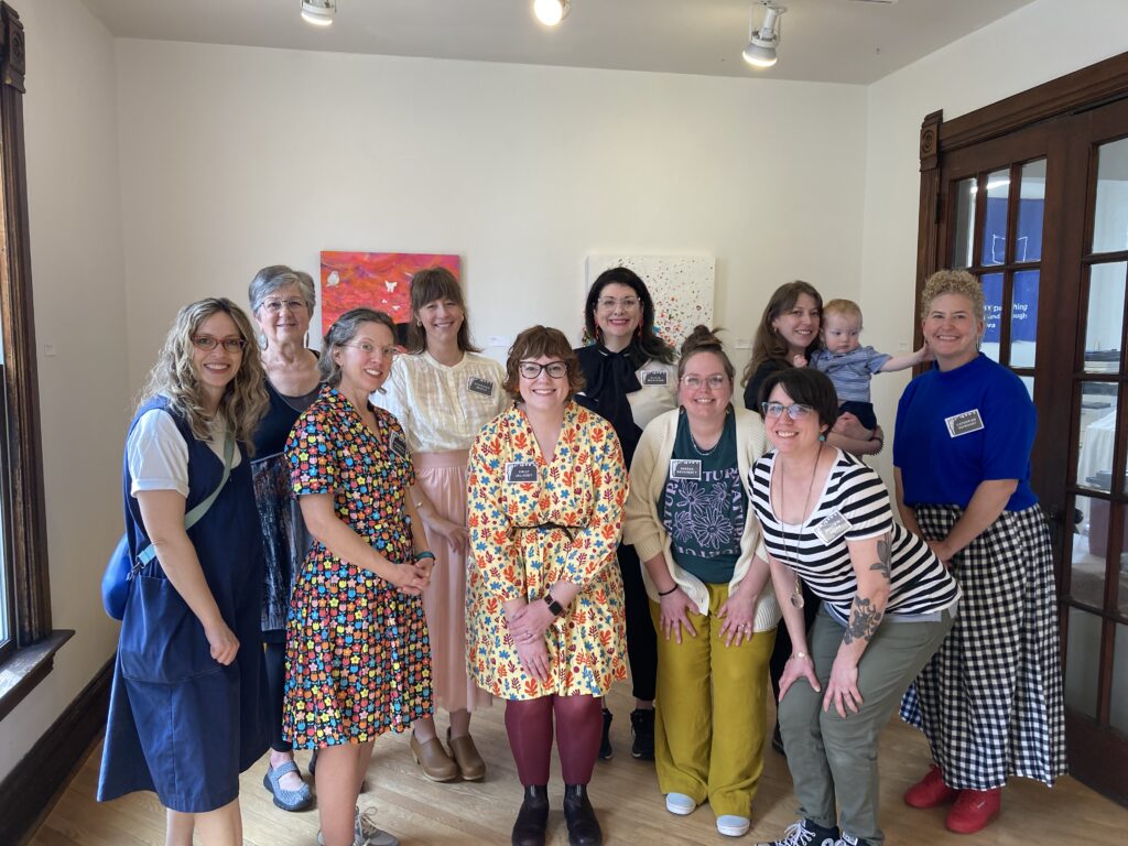 A group of women and one baby posing in an art gallery and smiling.