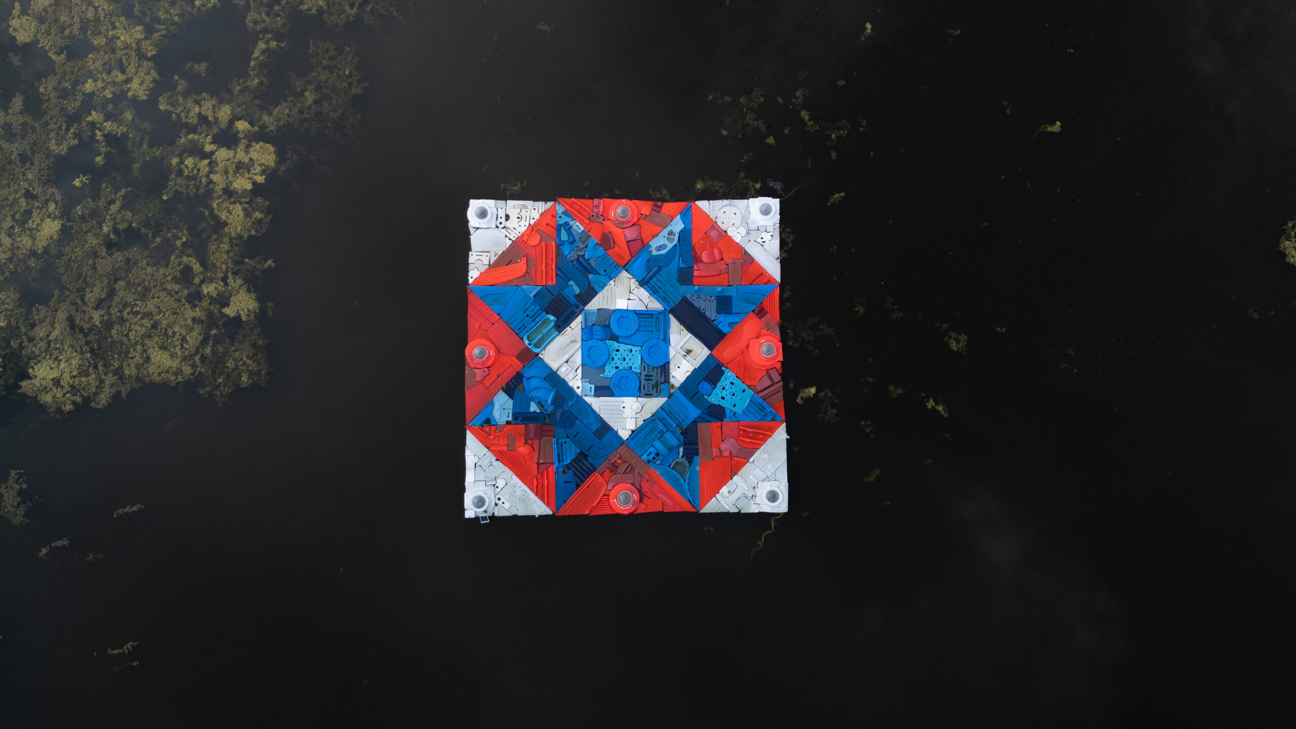 A floating sculpture on a pond depicting a large quilt pattern block.