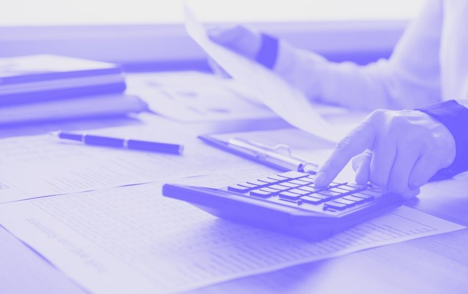 A person types on a calculator and reviews paperwork.