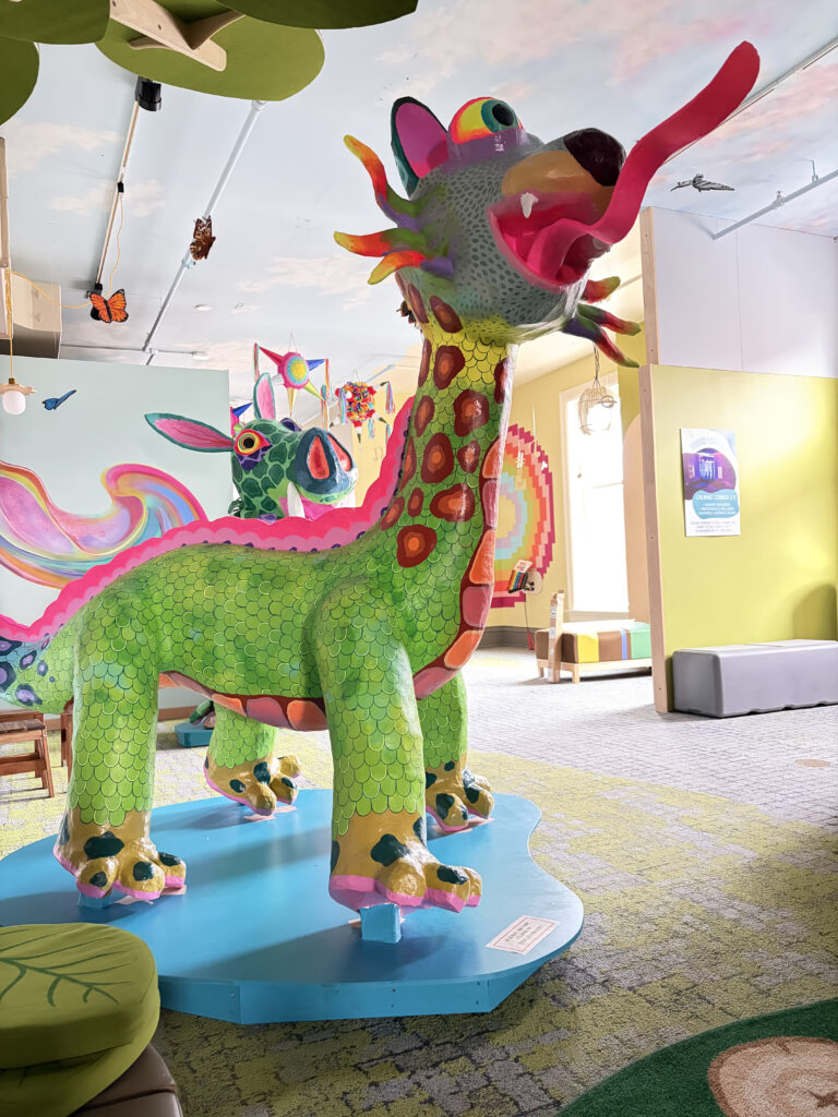 A large green, pink, and red multi-animal sculpture with a long next and long tongue.