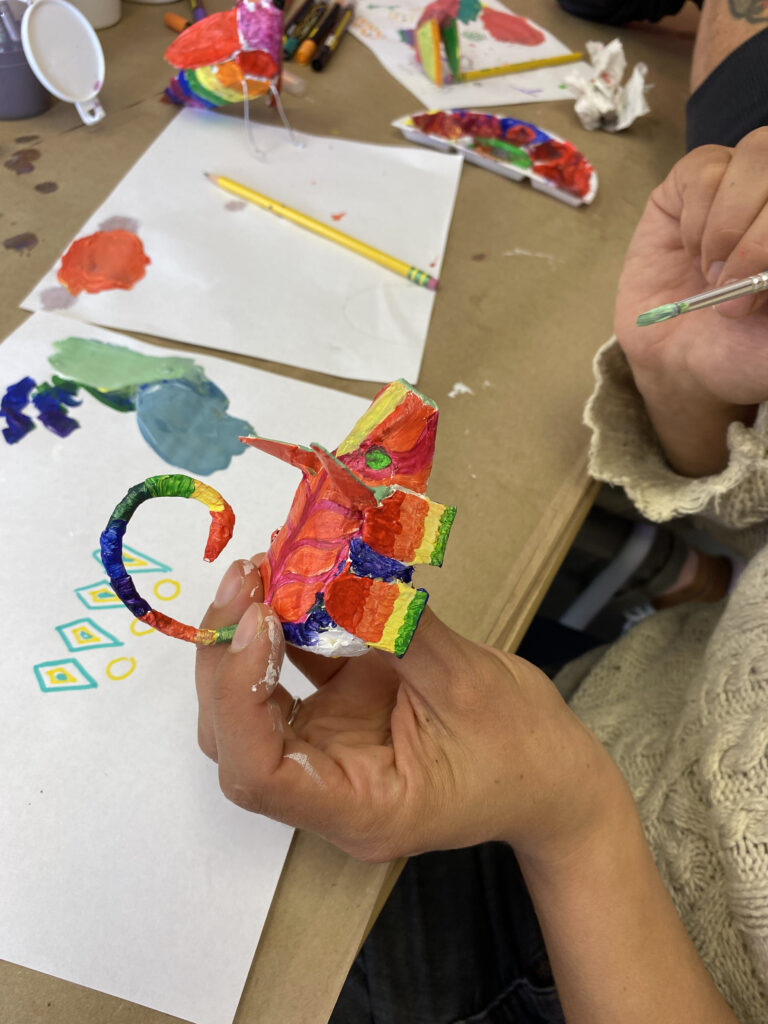 A person's hands painting a small animal sculpture.