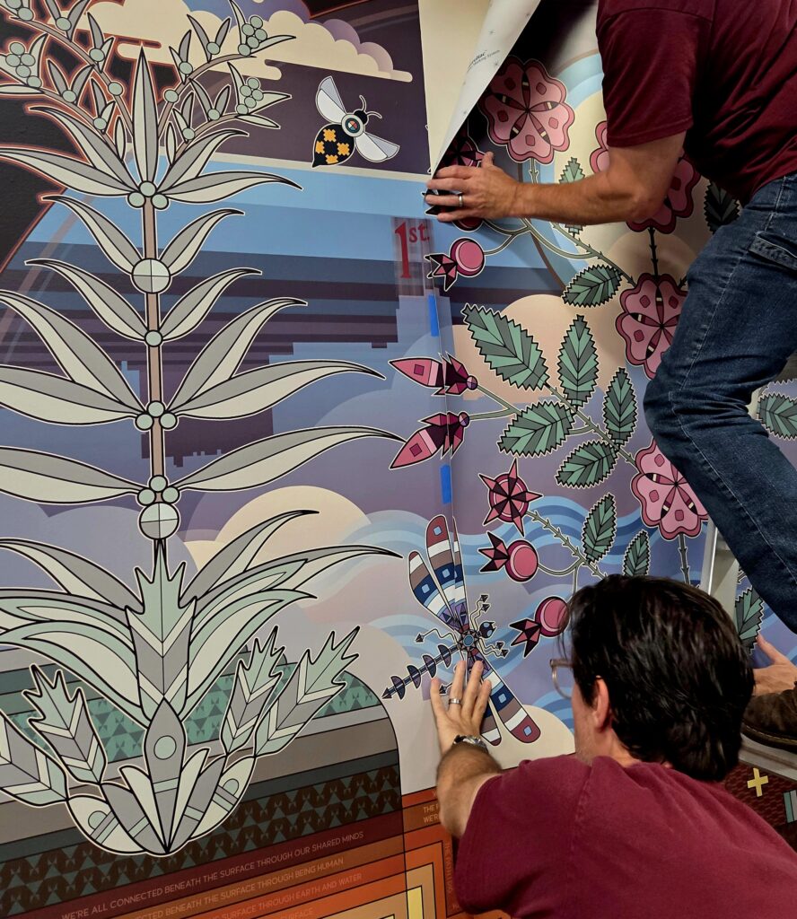 People pasting a vinyl mural to a large wall.