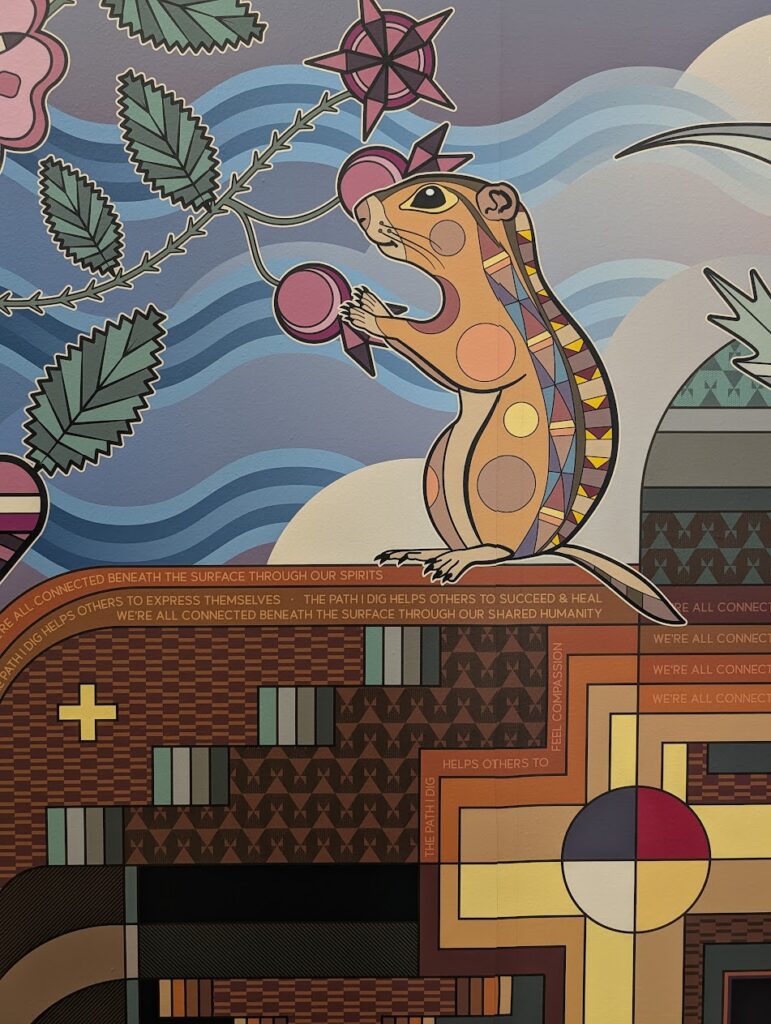 A closeup of a mural depicting a ground squirrel and plants, along with quotes from students.