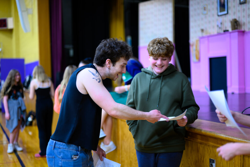 Two people happily review scripts in front of a dimly lit stage.
