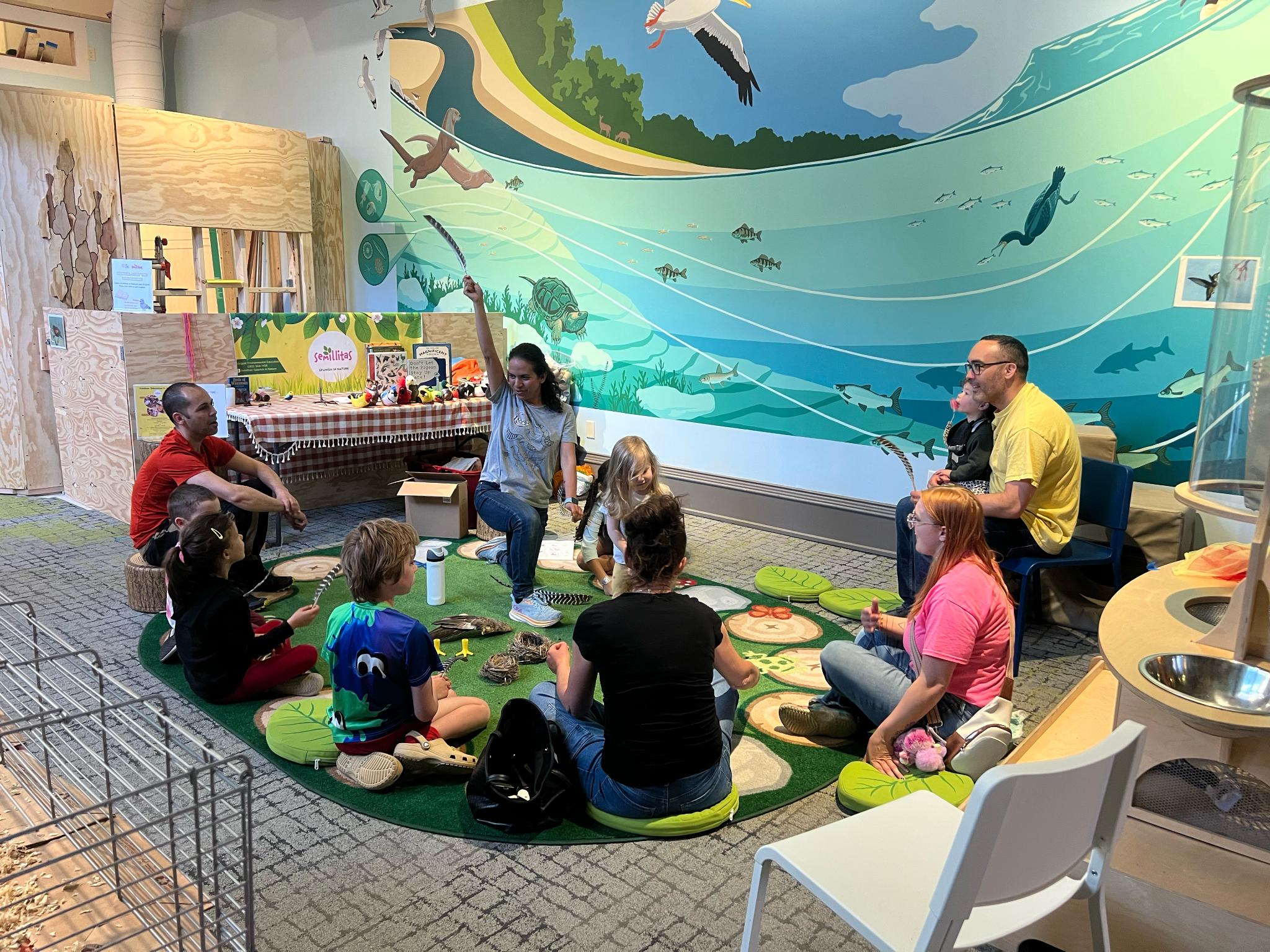 Families sitting in a circle under a colorful water mural telling stories.
