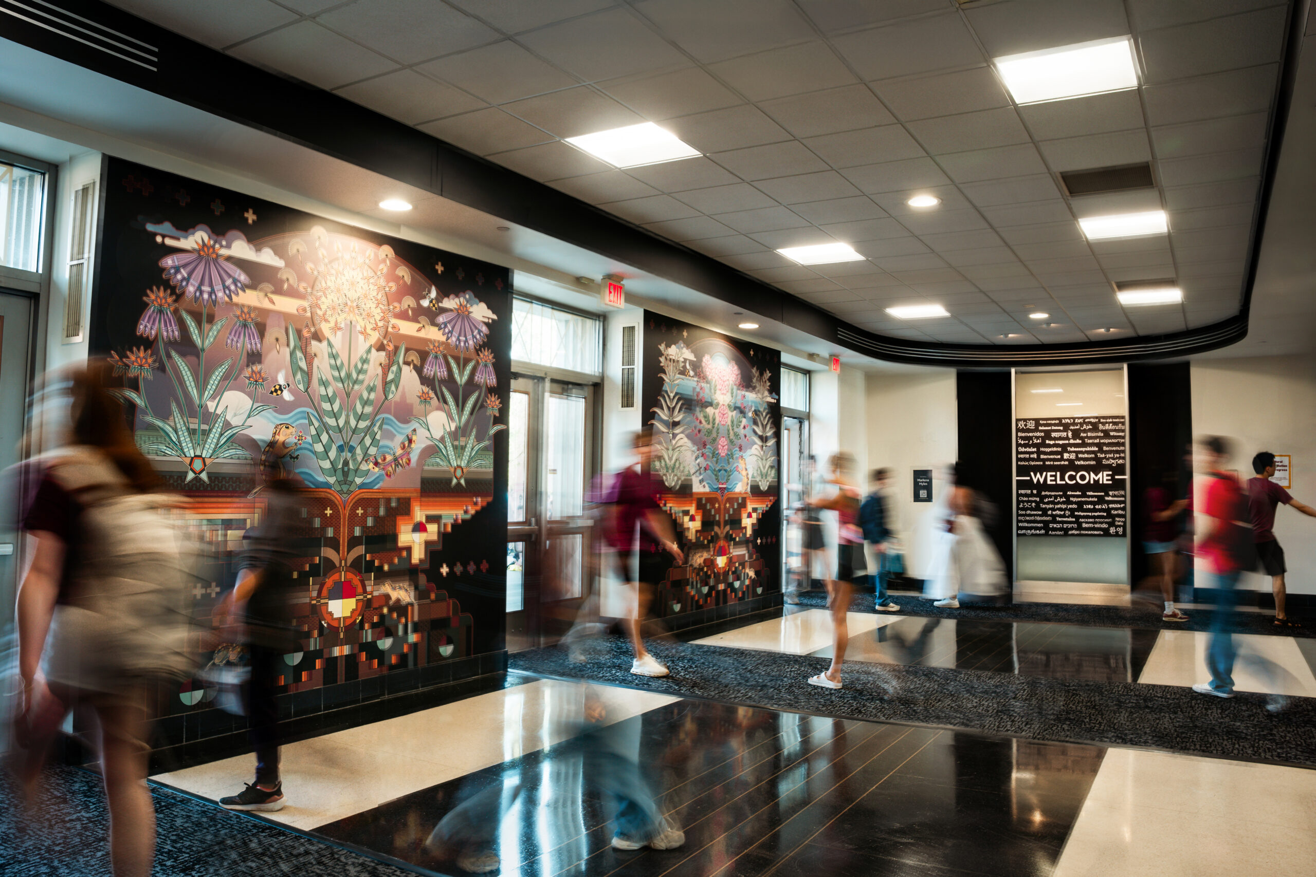 Blurred people walking in and out of an entryway with a welcome sign and murals.