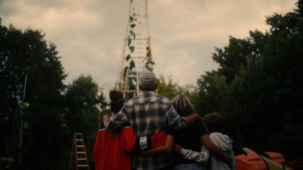 Four people facing away looking at a trellised flower and with arms wrapped around each other.