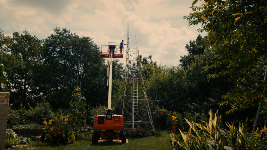 A person atop a tall mobile vehicle amid plants.
